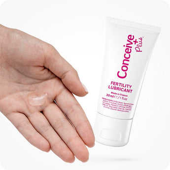 Conceive Plus Fertility Lubricant 30ml Tube shown beside an open palm with a small amount of clear gel applied from 30ml fertility lubricant multi-use tube, highlighting product's consistency and white packaging with pink labeling on white background.