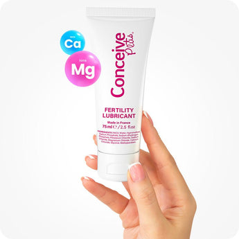 Conceive Plus Fertility Lubricant 75ml tube held upright between fingers with pink and blue Ca⁺ and Mg⁺ ion graphics floating nearby, visually emphasizing formula’s calcium and magnesium content designed for natural fertility support.