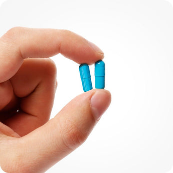 Conceive Plus Men's Fertility Support capsules held between two fingers, showing vibrant blue vegan capsules design close-up against white background, emphasizing ease of daily use and compact supplement size for male reproductive health.