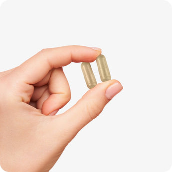 For Conceive Plus Motility and Ovulation Support Bundle, capsule size reference with a close-up of a hand gently holding two beige vegan capsules between thumb and index finger, shown against white background.